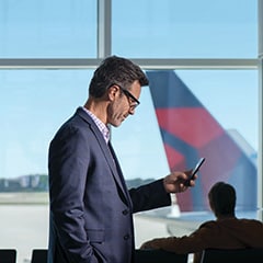 デルタ航空機の尾翼をバックに、空港で電話を操作しているビジネスマン